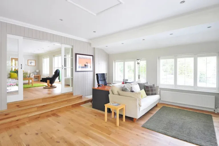 Living room interior with a modern couch, colorful rug, and sliding glass doors leading to a backyard.